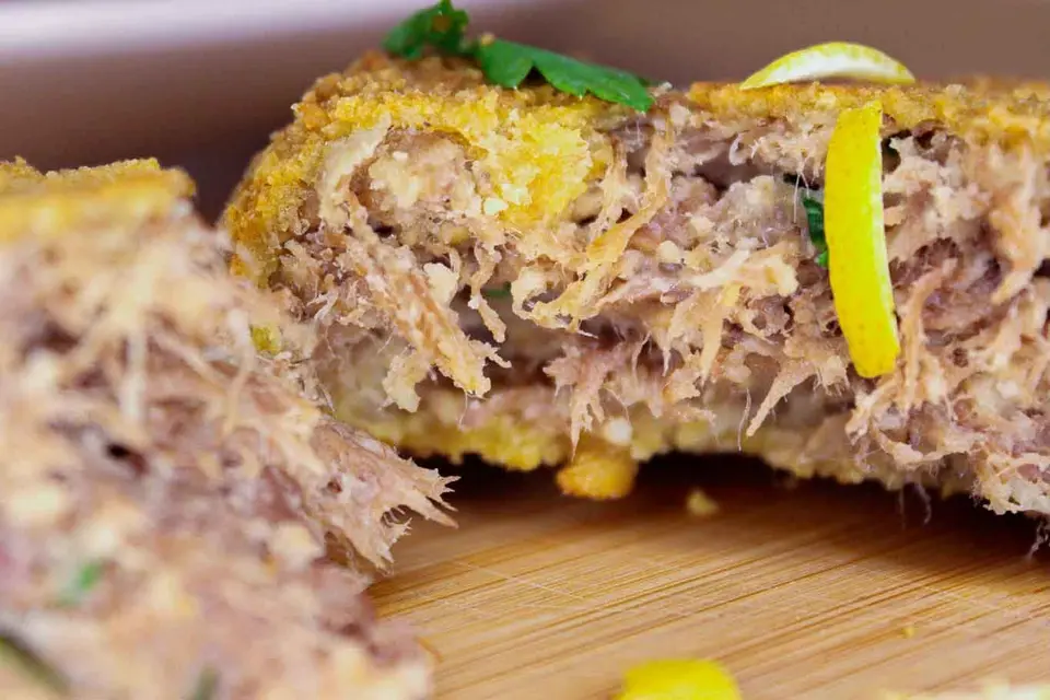 Polpetta di bollito impanata e fritta, aperta a metà, con scorza di limone e prezzemolo