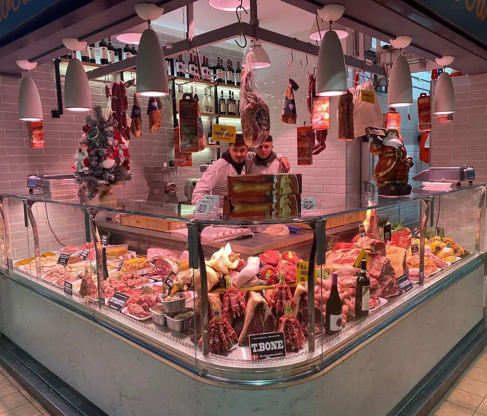 Il banco del Box 131 visto di fronte: la vetrina piena di carni, salumi appesi e Tiziano e Simone dietro al bancone